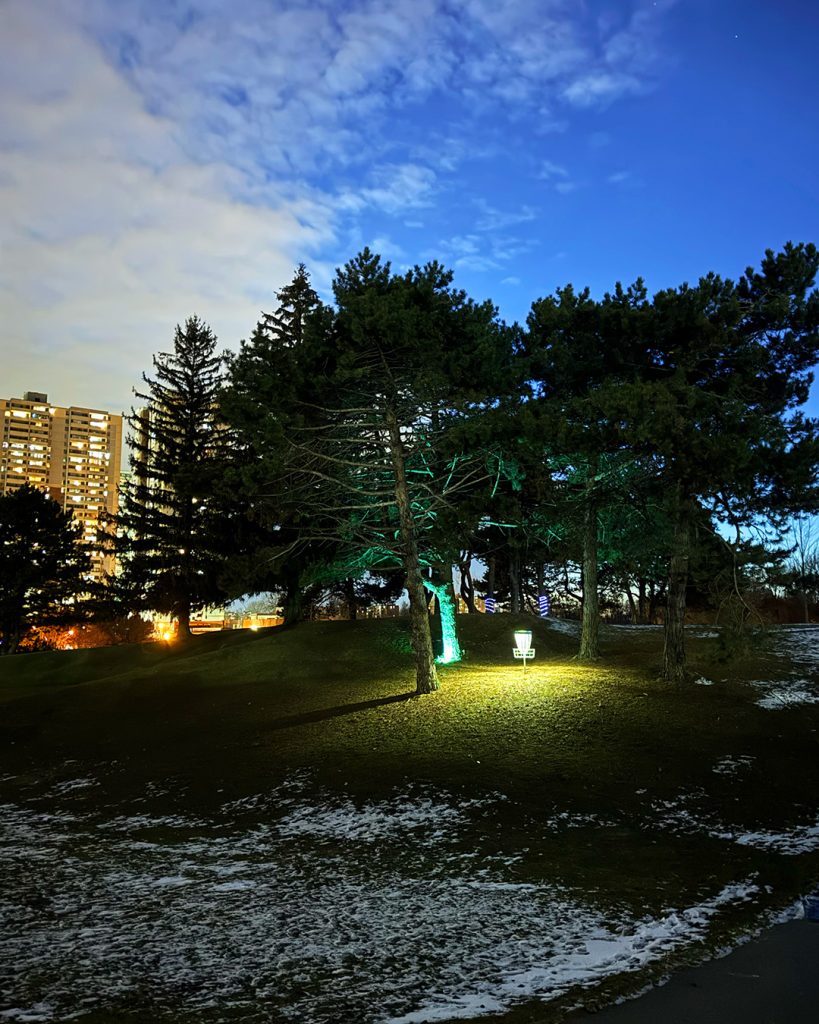 Disc golf basket glowing in the dark surrounded by green light during a Dr. Glow disc golf experience at the Toronto GLOWpen
