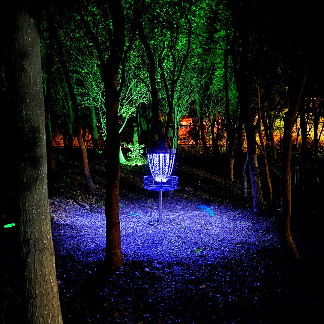 A disc golf basket illuminated with UV and glow lighting in the dark during the first ever glow disc golf round played in the Dominican Republic at Parque Central de Santiago.