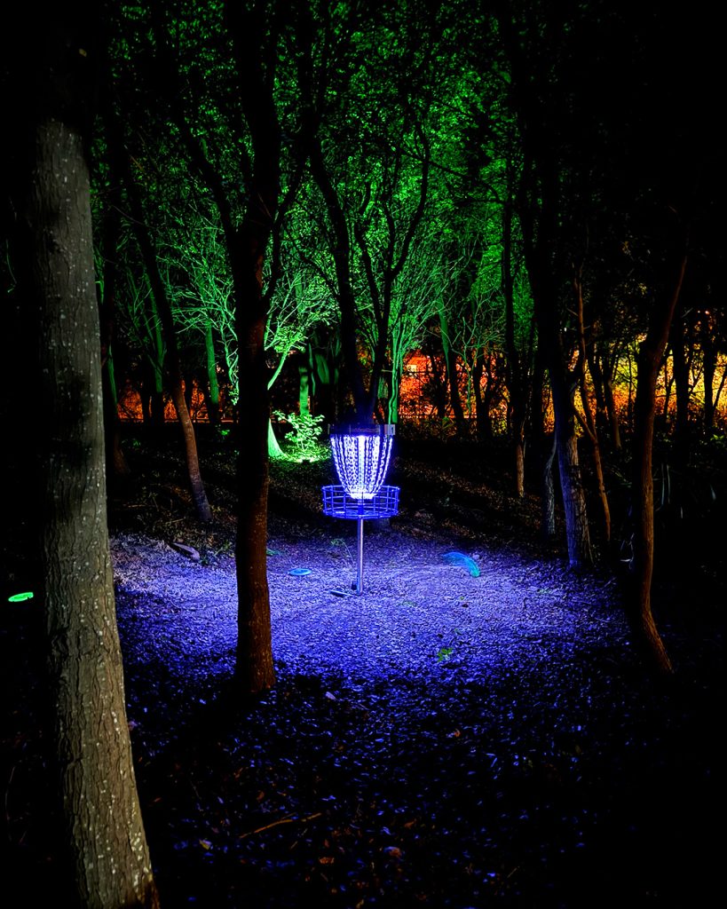 A disc golf basket illuminated with UV and glow lighting in the dark during the first ever glow disc golf round played in the Dominican Republic at Parque Central de Santiago.