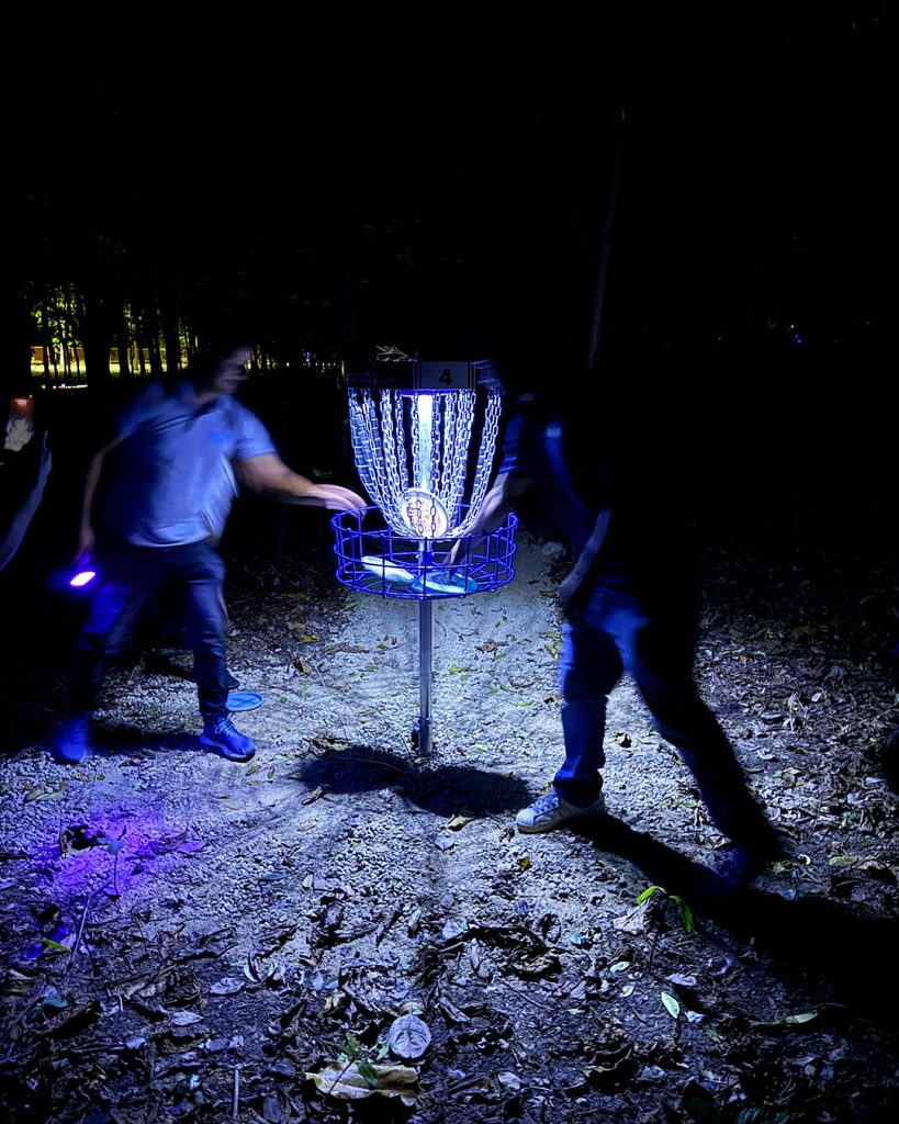 A disc golf basket illuminated with UV and glow lighting in the dark during the first ever glow disc golf round played in the Dominican Republic at Parque Central de Santiago.