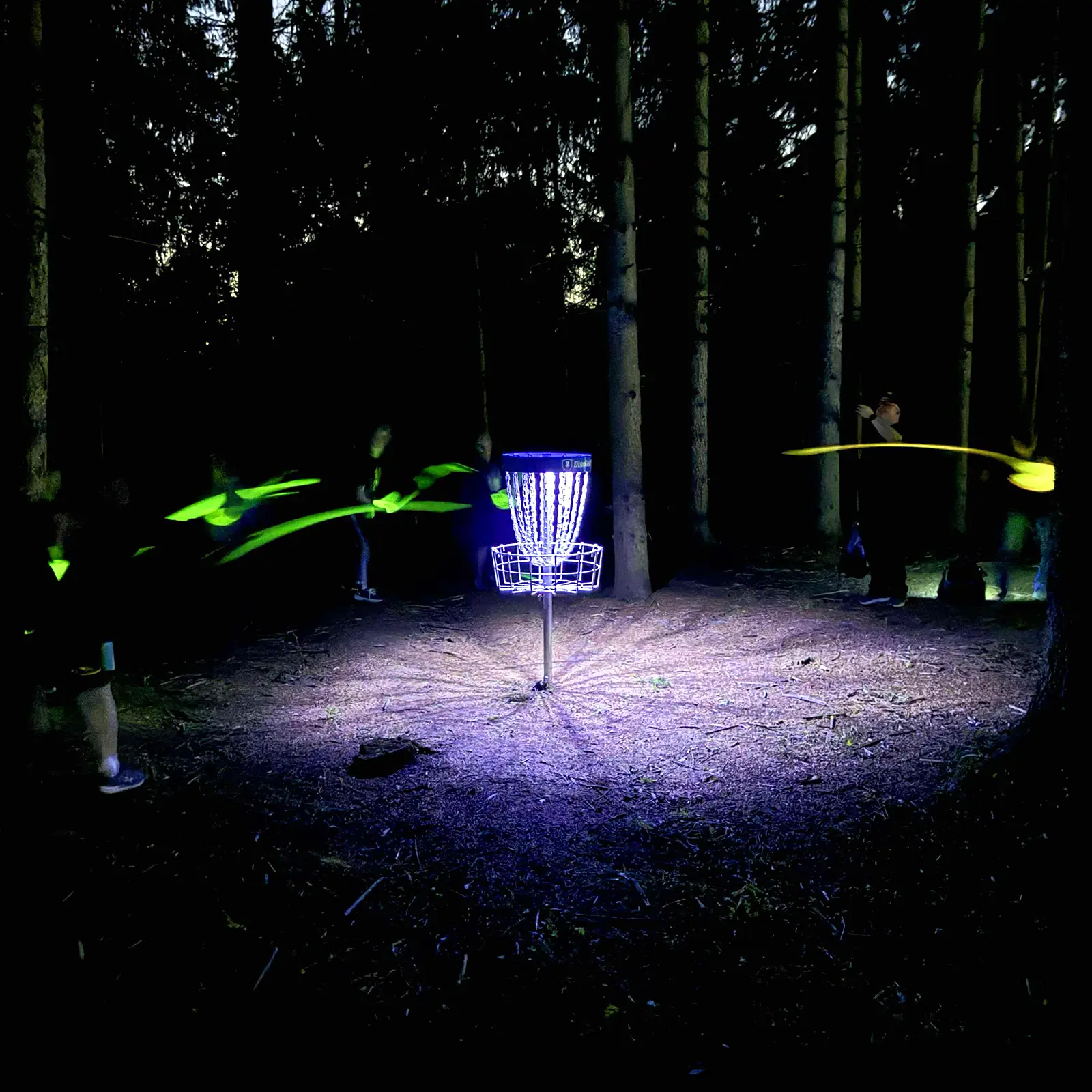 UFO UV basket light attached to disc golf basket, glowing purple at night