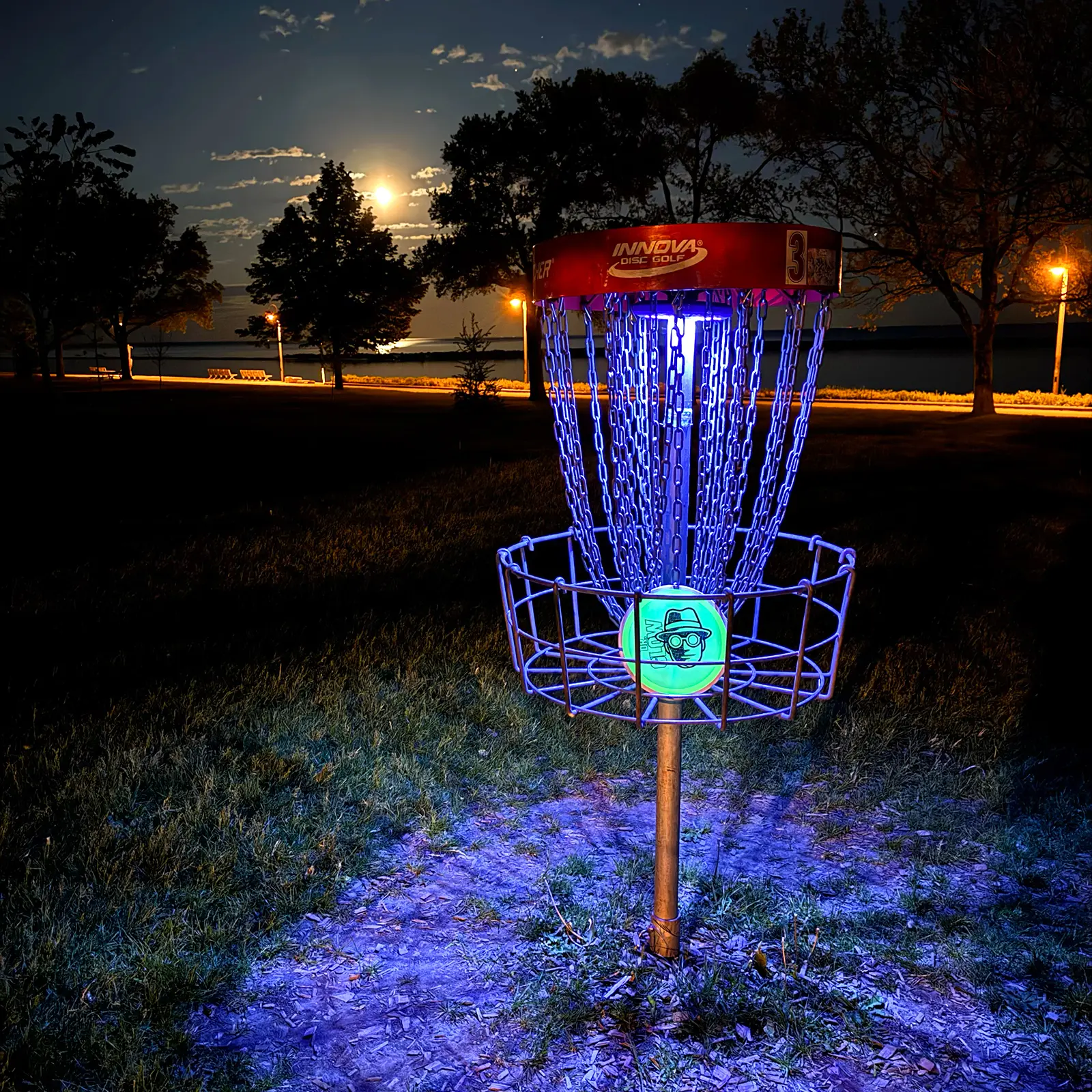 UFO UV basket light attached to disc golf basket, glowing purple at night