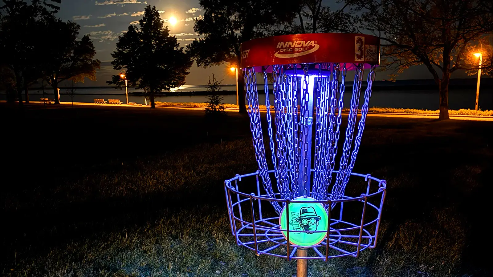 UFO UV basket light attached to disc golf basket, glowing purple at night