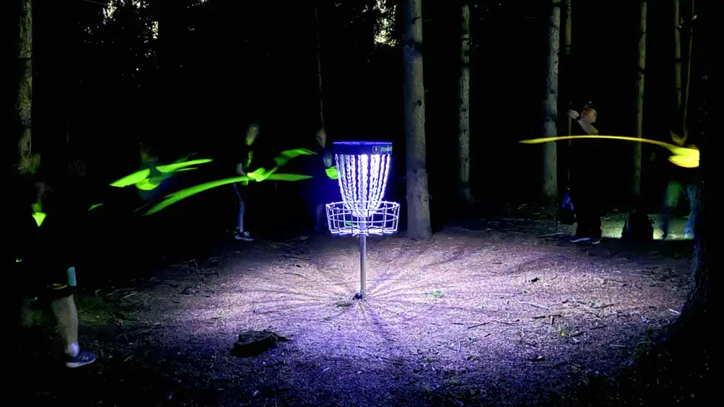 UFO UV basket light attached to disc golf basket, glowing purple at night