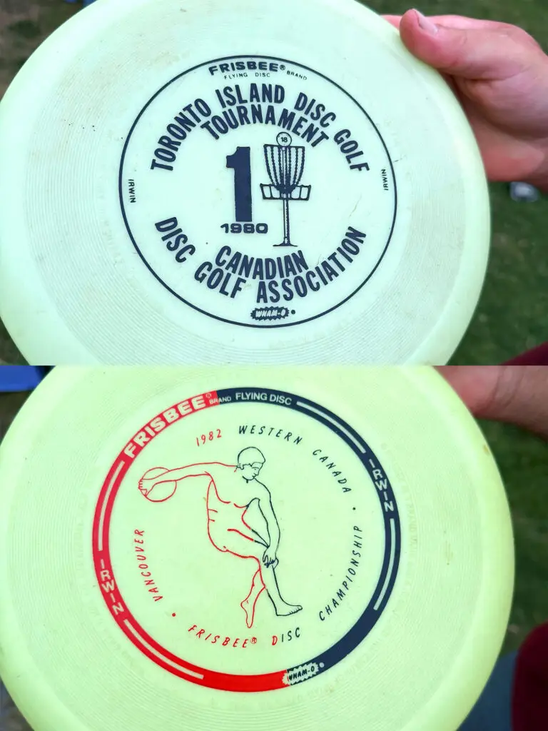 Two vintage glow-in-the-dark Frisbee brand discs, a 1980 Toronto Island Disc Golf Tournament disc and a 1982 Western Canada Championship disc from Vancouver.