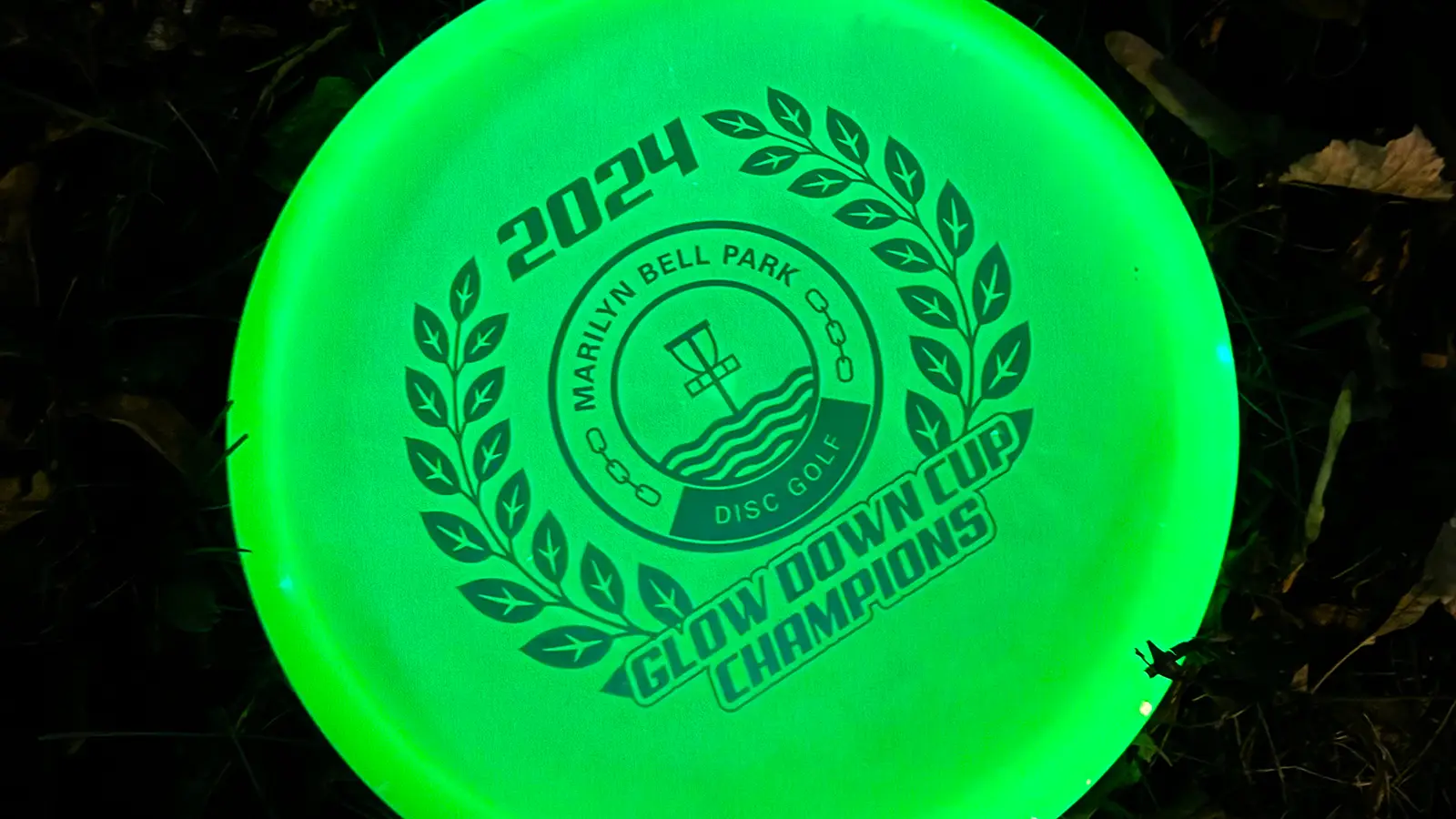 Glow-in-the-dark disc engraved "2024 Marilyn Bell Park Disc Golf, Glow Down Cup Champions"