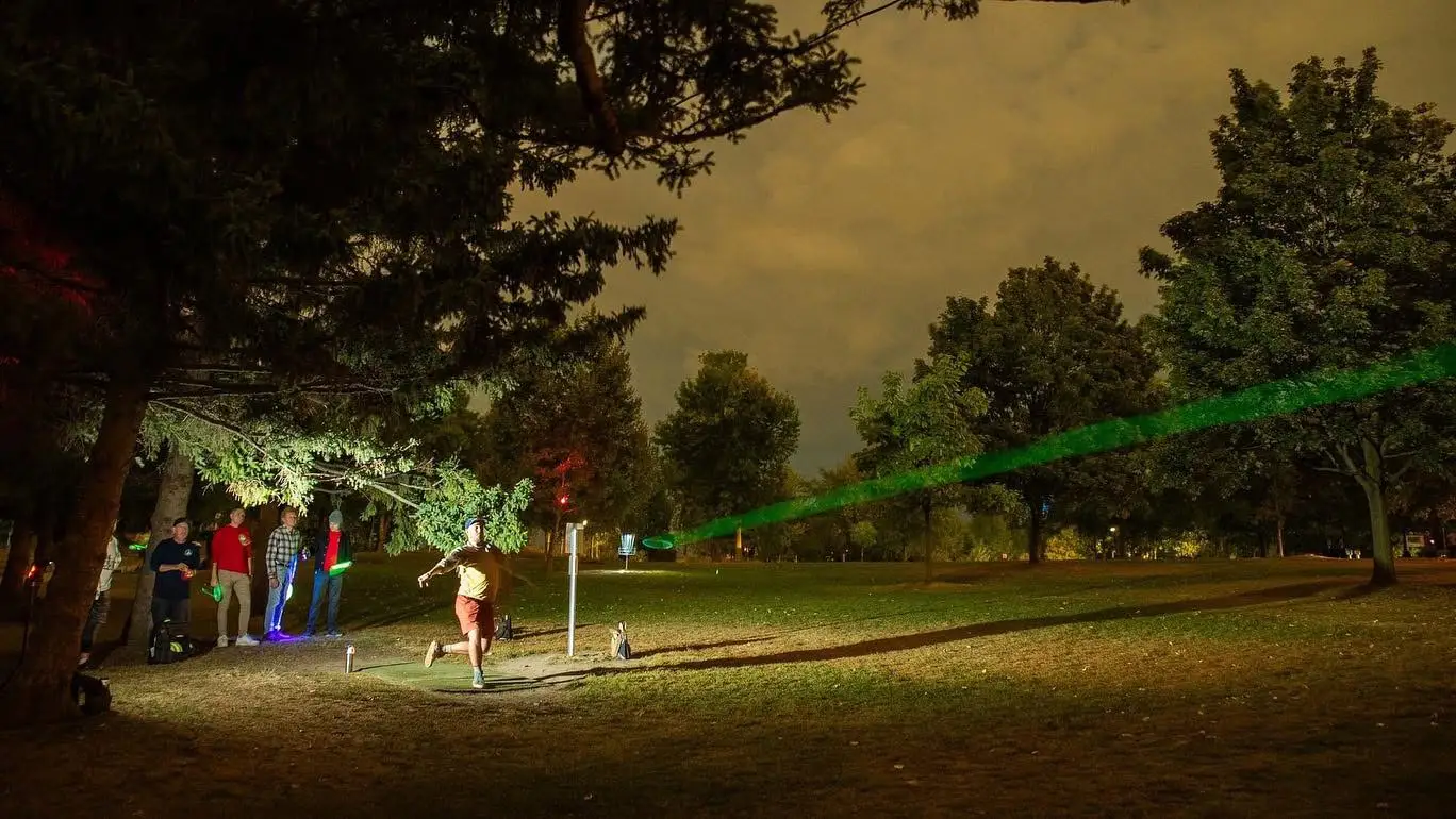 Disc golfer throwing a glow disc at night with a long exposure light trail