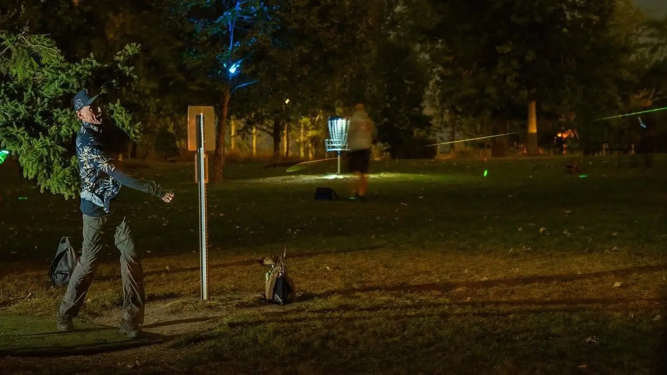 Disc golfer throwing toward a lit basket at night on a glow disc golf course