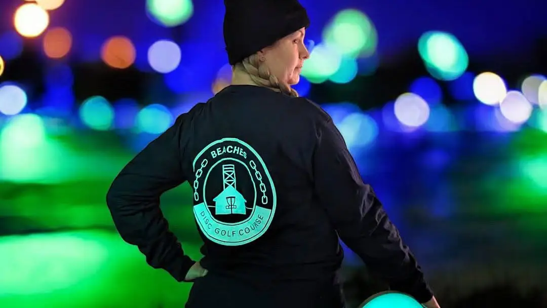 Team Beaches disc golf player holding a glowing disc with Toronto city lights in the background