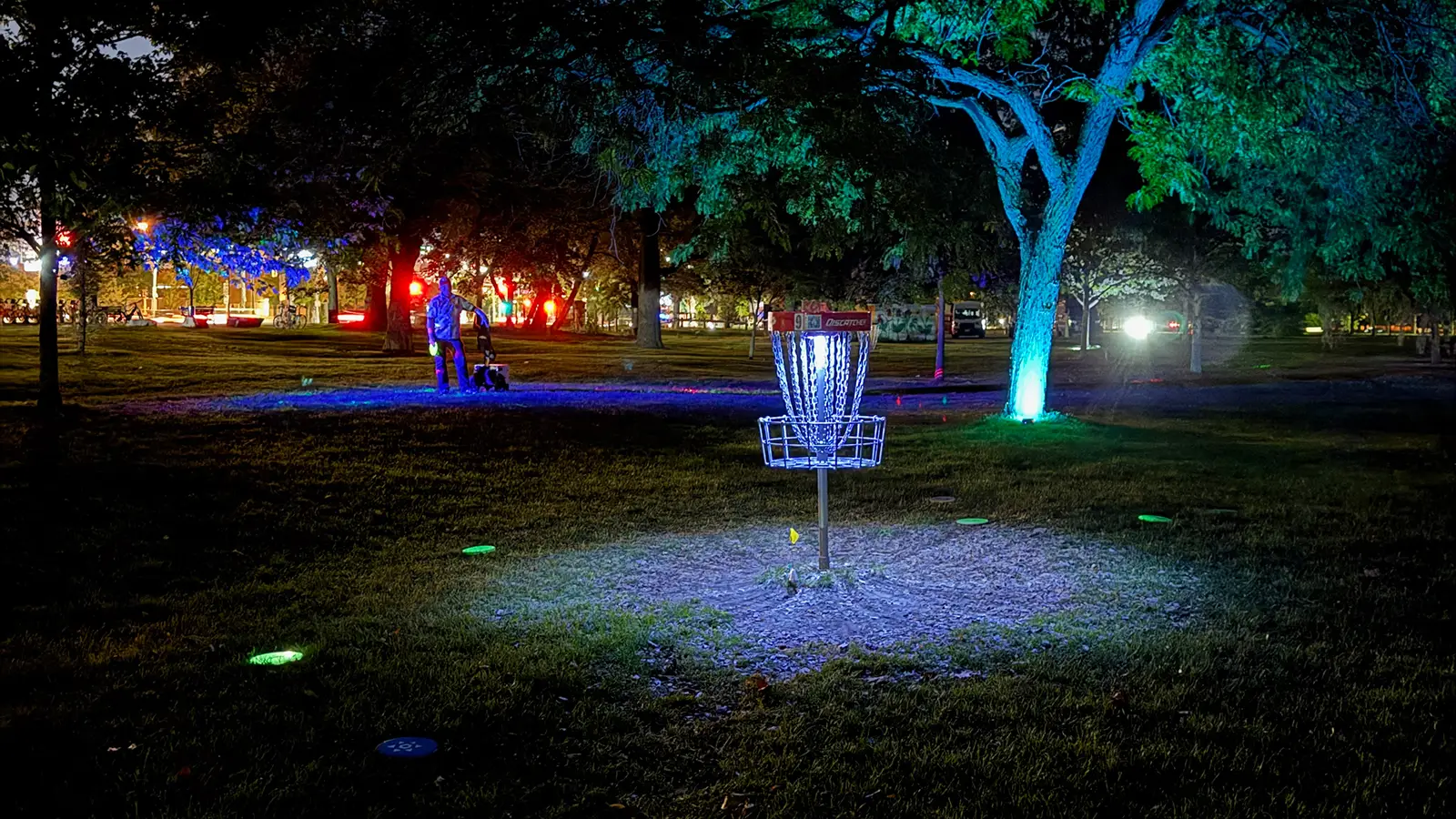 Illuminated disc golf basket glowing under trees at night on a Toronto glow disc golf course