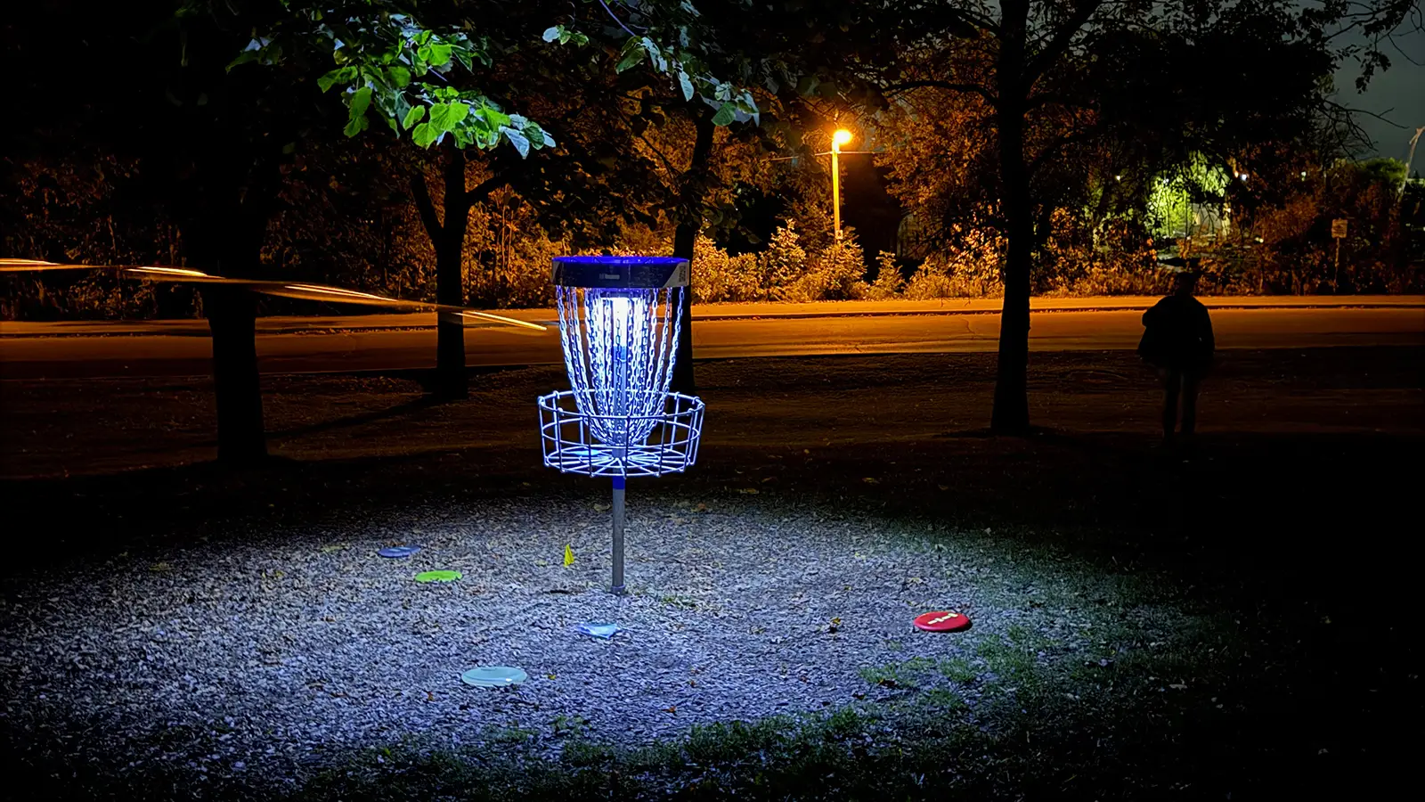 Glowing disc golf basket at night with scattered glow discs on the fairway