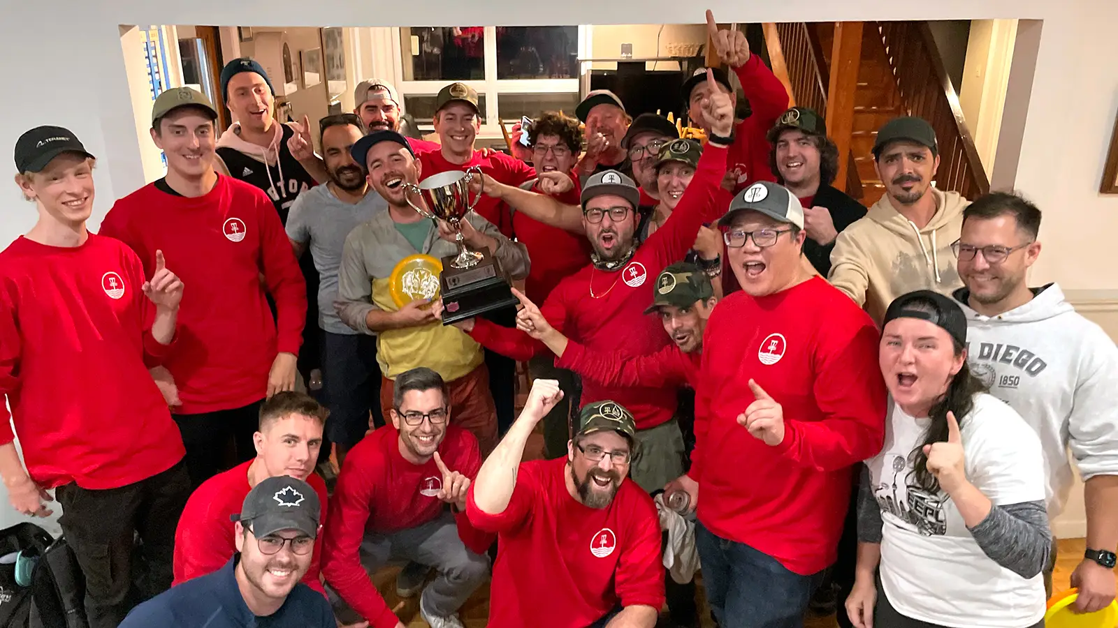 Team Bell disc golf players in red shirts celebrating with the Glow Down Cup trophy indoors