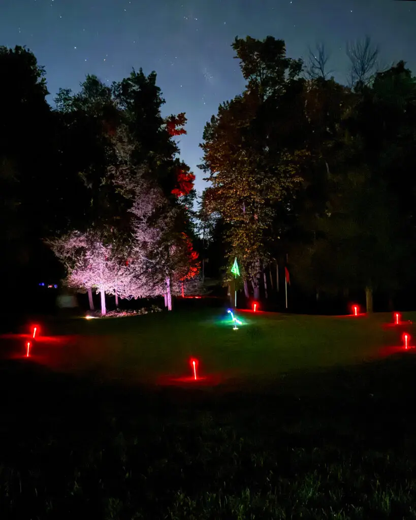 Red LED tee markers surround a green with a glowing green flag, framed by a white frosted tree and red-lit trees at Black Bear Ridge.