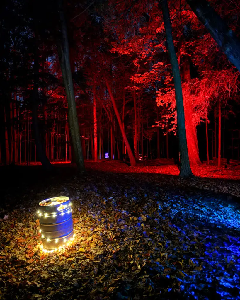 A string-light-wrapped keg glowing in a forest lit completely red, with a basket faintly visible down the path