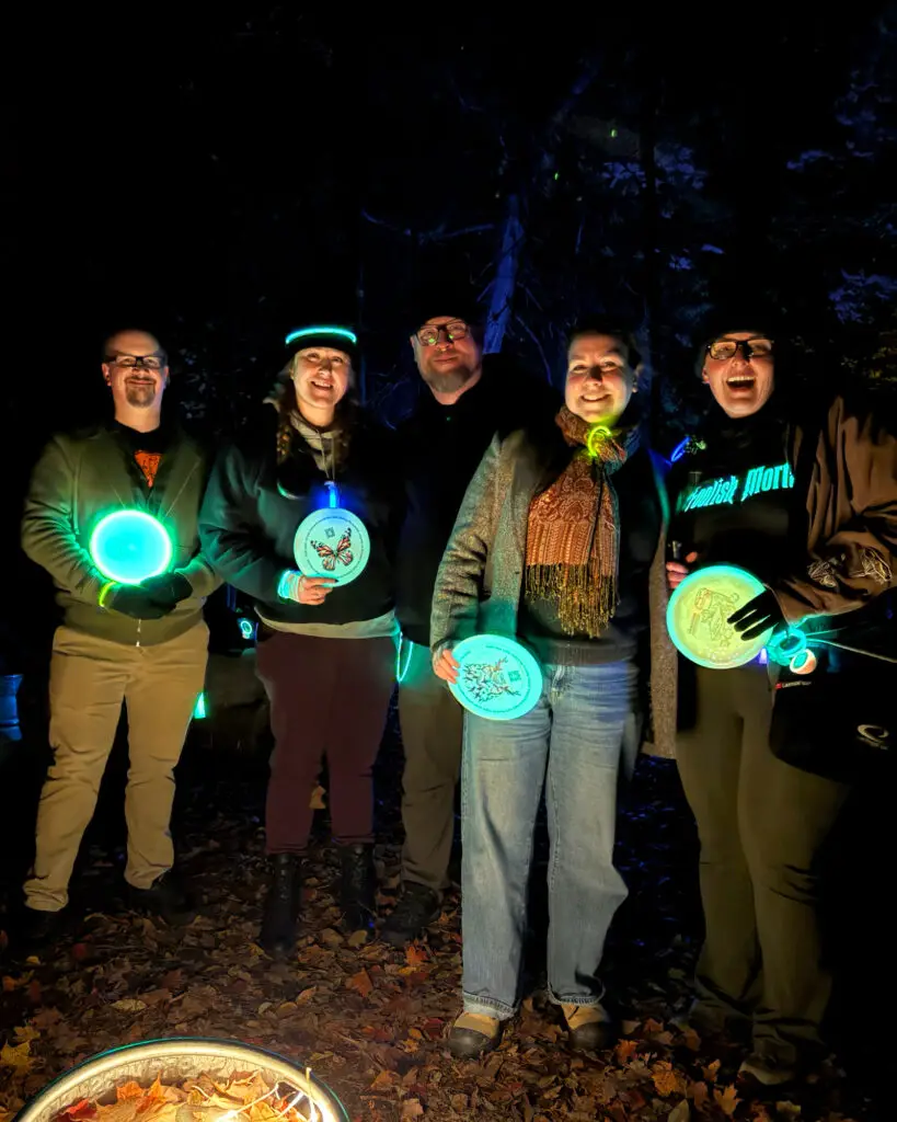Five GLOWLOT players laughing together while holding glowing discs, with a lit keg visible nearby